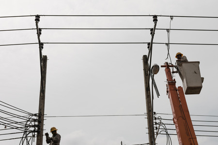 Bangkok, Thailand - August 5, 2017: Electrician working on electric pole at an altitude to installs cable high voltage against to transformer with cloudy sky. のeditorial素材