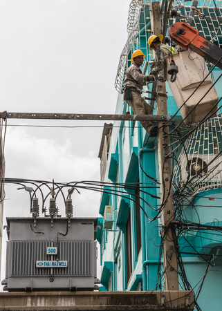 Bangkok, Thailand - August 5, 2017: Electrician working on electric pole at an altitude to installs cable high voltage against to transformer with cloudy sky. のeditorial素材