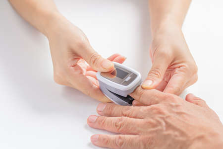 Female hands measures the patient's pulse and oxygen saturation (SPO2) for middle aged man using a...