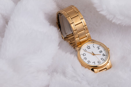 Luxury wristwatch made of a gold-toned metal on a white background, with depth of field.