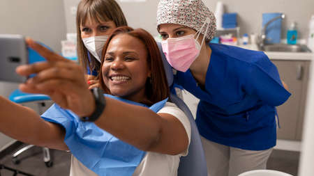 A black woman patient takes a selfie with two dentist woman at the dental clinicの写真素材
