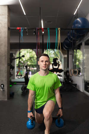 A young man doing split squat, and holding the kettlebells