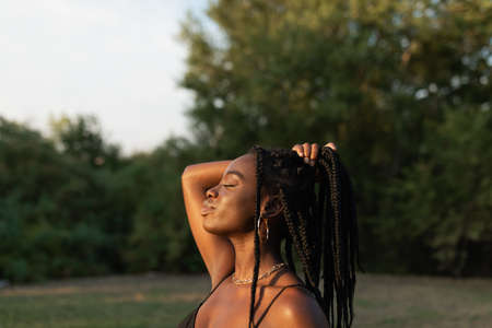 Side view of a young black female holding her braids with her hand in a ponytail with closed eyes at the parkの写真素材