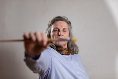 Mature artist woman eye measuring with on of her brushesの写真素材