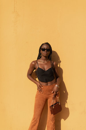 Portrait of a young black female posing with style with a plain orange wall behind herの写真素材