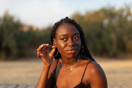 Close-up portrait of a young black female touching her lobe in the park
