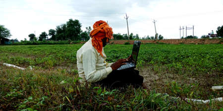 District Katni, Madhya Pradesh, India - 28 August 2019: An indian male farmer operating laptop around natural field at open background.のeditorial素材