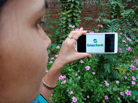 DISTRICT KATNI, INDIA - JUNE 02, 2020: An indian woman holding smart phone with displaying Sviaz Bank Russia logo on screen, modern islamic banking education concept for village people.のeditorial素材