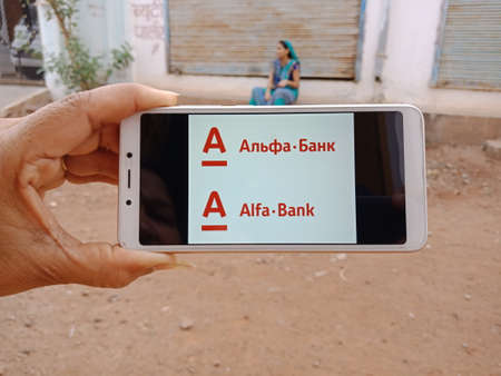 DISTRICT KATNI, INDIA - JUNE 02, 2020: An indian woman holding smart phone with displaying Alfa Bank Private banking company logo on screen, modern banking education concept for village people.のeditorial素材