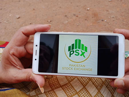 DISTRICT KATNI, INDIA - JUNE 02, 2020: An indian woman holding smart phone with displaying Pakistan Stock Exchange logo on screen, modern islamic banking education concept for village people.のeditorial素材