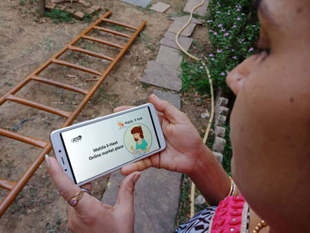 DISTRICT KATNI, INDIA - 28 MAY 2020: An indian lady holding smart phone with displaying mahila e haat online market place on screen, modern business education concept for village woman people.のeditorial素材
