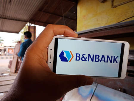 DISTRICT KATNI, INDIA - JUNE 02, 2020: An indian man holding smart phone with displaying B and N Bank Commercial bank logo on screen, modern russian banking education concept for village people.のeditorial素材