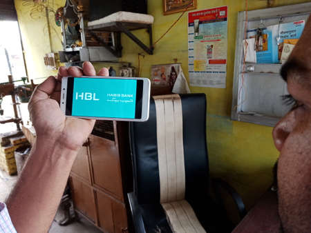 DISTRICT KATNI, INDIA - JUNE 02, 2020: An indian man holding smart phone with displaying Habib Bank Limited logo on screen, islamic banking education concept for village people.のeditorial素材