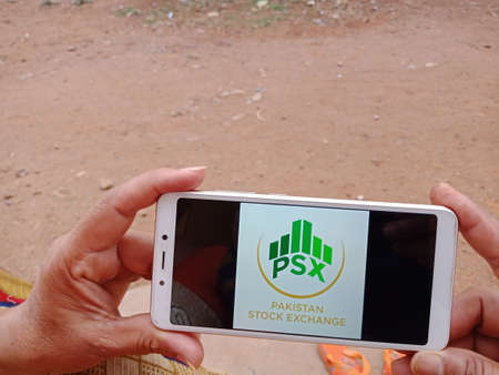 DISTRICT KATNI, INDIA - JUNE 02, 2020: An indian woman holding smart phone with displaying Pakistan Stock Exchange logo on screen, modern banking education concept for village people.のeditorial素材