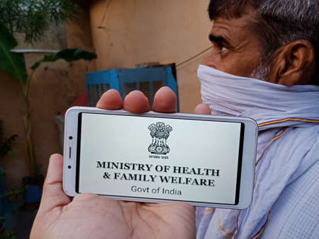 DISTRICT KATNI, INDIA - 28 MAY 2020: An indian village Man holding smart phone with displaying ministry of health and family welfare logo on screen, initiated by government of India.のeditorial素材