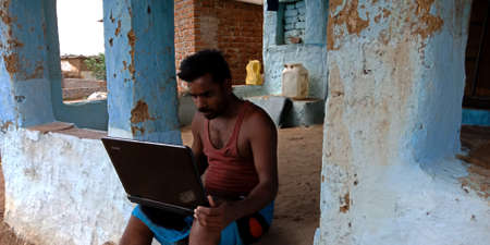 DISTRICT KATNI, INDIA - AUGUST 16, 2019: An indian village man working on laptop at open area. Villager technology learning concept.のeditorial素材