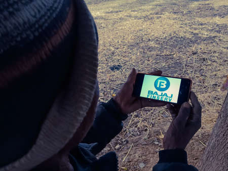 DISTRICT KATNI, INDIA - DECEMBER 20, 2019: Bajaj Finserv Ltd.Financial services company logo presented on smart phone digital screen by indian village people hand holding mobile concept.のeditorial素材