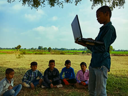 DISTRICT KATNI, INDIA - JANUARY 01, 2020: An indian boy giving training about laptop technology to the group of kids at open area ground.のeditorial素材