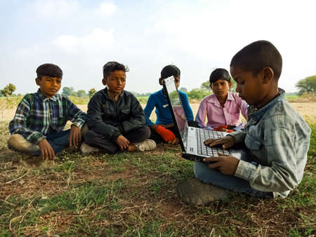 DISTRICT KATNI, INDIA - JANUARY 01, 2020: An indian poor boy teaching about laptop technology to the group of kids at open area green field.のeditorial素材