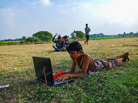 DISTRICT KATNI, INDIA - JANUARY 01, 2020: An indian male kid lying on the green land while operating laptop computer at open area environment.のeditorial素材