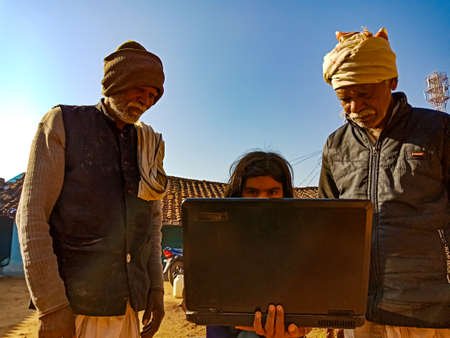 DISTRICT KATNI, INDIA - JANUARY 25, 2020: An indian girl giving training about laptop technology to old farmer man together at sky background.のeditorial素材