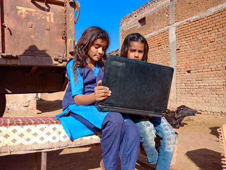 DISTRICT KATNI, INDIA - JANUARY 25, 2020: Two indian village school girls learning together about laptop at brick wall open area background.のeditorial素材