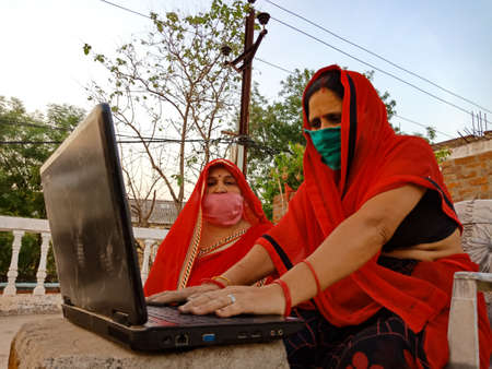 DISTRICT KATNI, INDIA - MAY 23, 2020: An indian woman learning laptop technology at open area background wearing face mask for corona virus protection.のeditorial素材