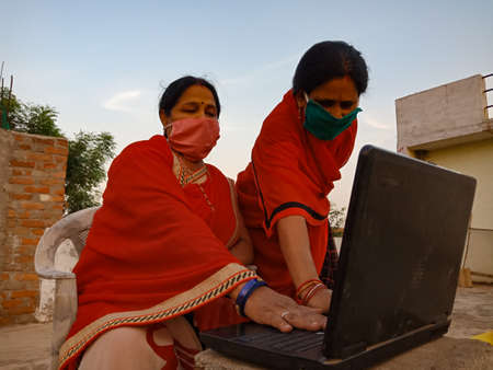 DISTRICT KATNI, INDIA - MAY 23, 2020: An indian woman giving training to the poor lady wearing face cover for coronavirus protection, digital india concept presented.のeditorial素材