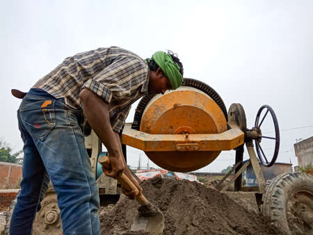 DISTRICT KATNI, INDIA - DECEMBER 18, 2019: An indian village male labour mixing cemented building material at home construction site.のeditorial素材