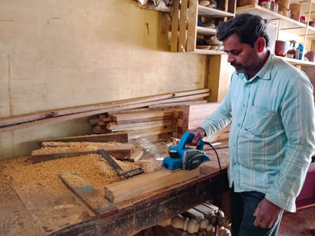 DISTRICT KATNI, INDIA - JANUARY 08, 2020: An asian male woodworker chopping wooden log from electric...