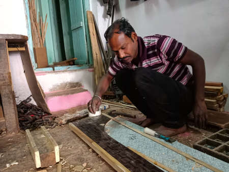 DISTRICT KATNI, INDIA - JANUARY 08, 2020: An indian wooden artist applying fevicol liquid for affixing wood log at furniture workshop.のeditorial素材