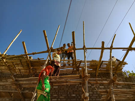 DISTRICT KATNI, INDIA - JANUARY 18, 2020: Group of asian village labours creating wall wooden structure at building construction site in sky background.のeditorial素材