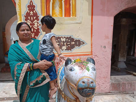 DISTRICT KATNI, INDIA - JULY 08, 2020: indian village woman carried cute kid on lap while worshiping at hindu holy temple, tour and travel with family concept.のeditorial素材