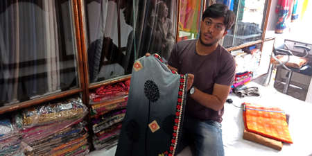 DISTRICT KATNI, INDIA - SEPTEMBER 22, 2019: An indian shopkeeper presenting Beautiful Sari outfit into the traditional clothes store at local city market.のeditorial素材