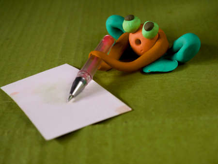 Funny clay frog holding pen writing on white card education concept