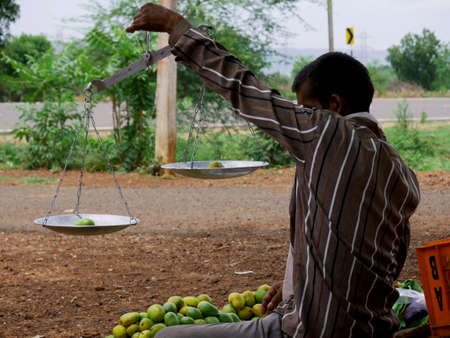 Street fruit seller weight measuring of fresh organic mango on hand.