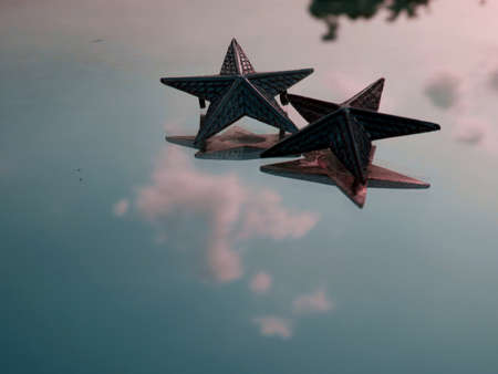 Double metal star presented on glass surface with sky reflection.の写真素材