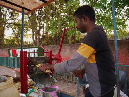 DISTRICT KATNI, INDIA - MARCH 02, 2022: An asian poor man operating sugarcane juicer machine with hard work at green plant background day time.のeditorial素材