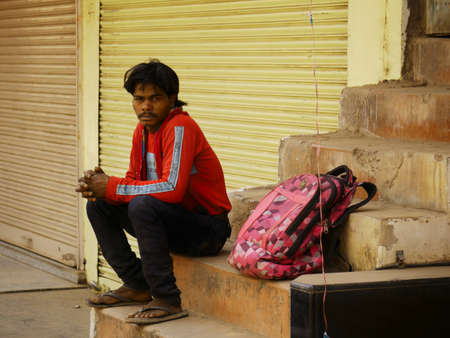 An indian village poor man sitting alone at outside of closing shop stairs while keeping luggage...