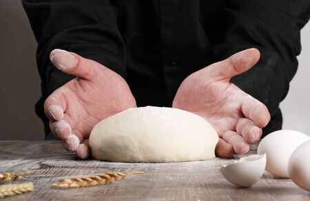 chef hands kneading the dough and eggs, ears wheat on wood table 