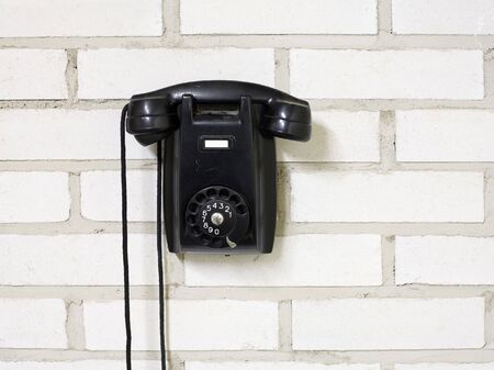Black bakelite telephone on a brick wall.