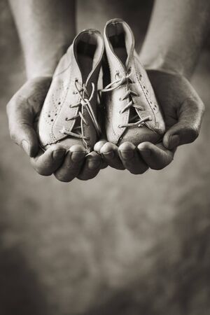 Dirty hands holding a pair of baby shoes. Very shallow depth of field.の写真素材