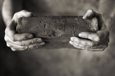 Sepia toned photo of DIrty hands holding an old brickの写真素材