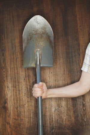 Man holding a spade in front of wooden background.の写真素材