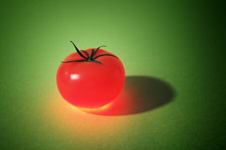 A Glowing Tomato on green background. Note that the background may appear noisy, but it's just the structure of the paper.の写真素材