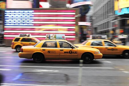 NEW YORK CITY, USA - JUNE 12: Yellow taxi cab speeding through Times Square. A US flag in the...