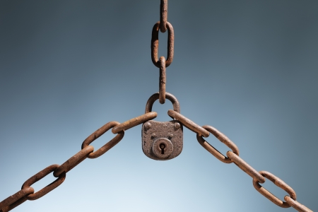 Old rusty lock holding three rusty chains together.の写真素材