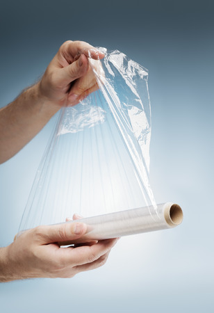 Man holding a roll of plastic film, typically used for sealing food items.の写真素材
