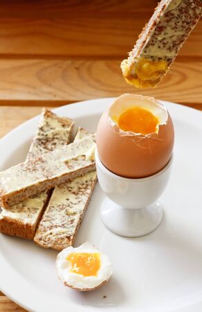 A buttered toast soldiers being dipped into a soft boiled egg in an egg cupの写真素材