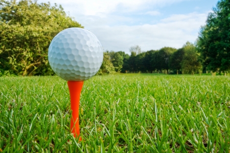 Golf ball on tee with fairway, golf course and flag in distanceの写真素材